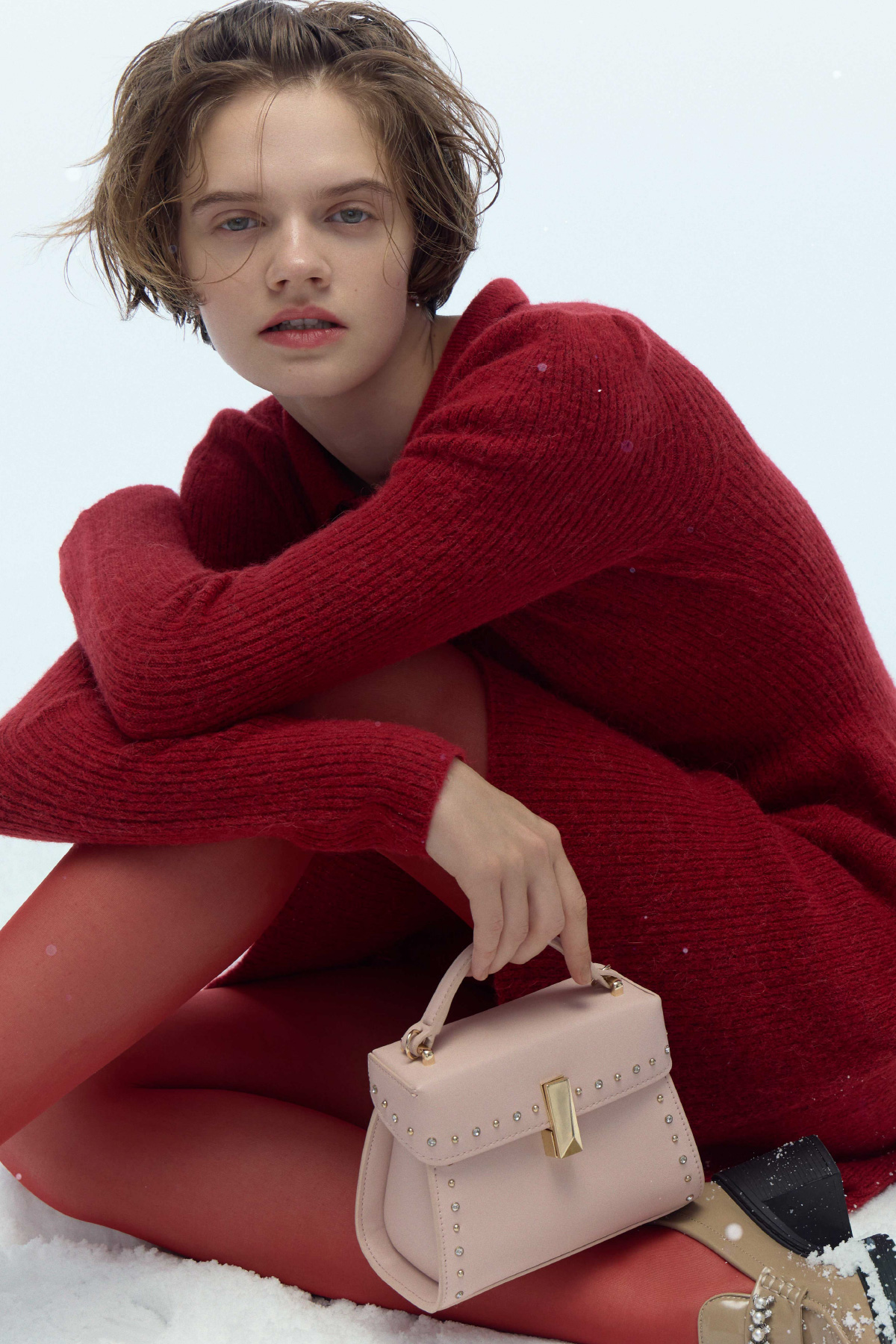 襟付きミニニットワンピース、ビジューリボンイヤリング、リュタンビジュースタッズポシェット、ビジューパール付き厚底ローファーを着て座ってるモデル画像