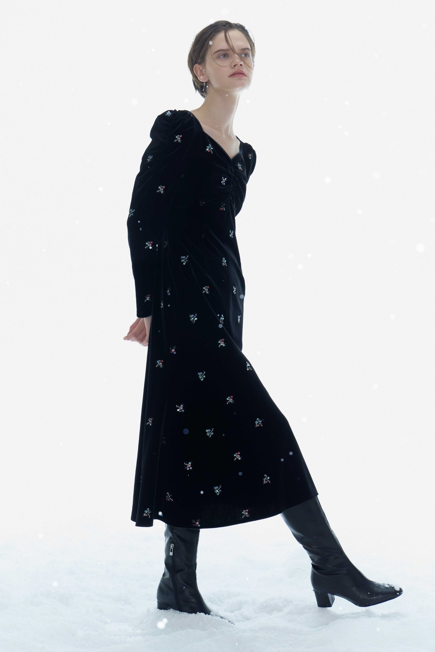 ブラック色の花柄刺繡ベロアワンピースとロゴメタル付きロングブーツを着用した女性のイメージ