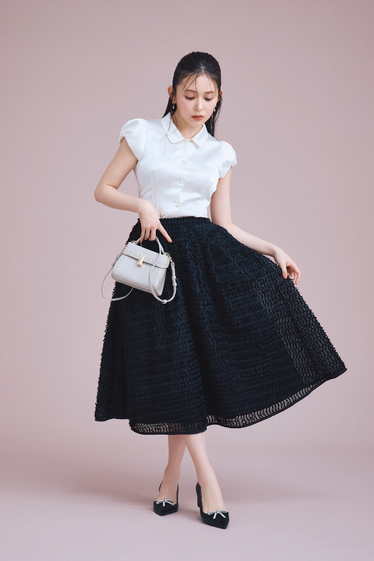 白色のフロントスカラサテンブラウスとブラック色のリボンジャガードタックフレアスカートを着用したモデル画像