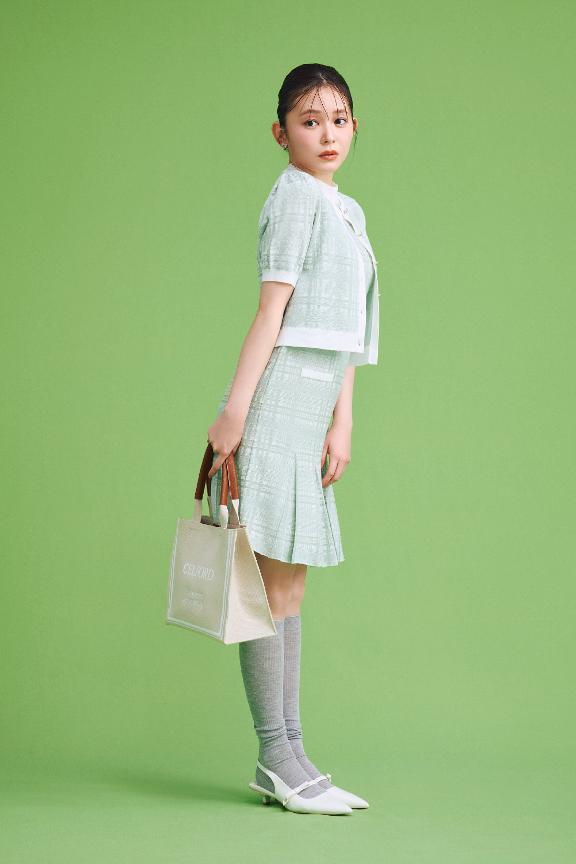 【WEB限定カラー】チェックジャカードニットワンピースセット、リボンビジューイヤリング、CELFORDロゴニットバッグ、ロゴ刺繍入り靴下、リボンディテールバックストラップミュールを着用した女性の横すがた