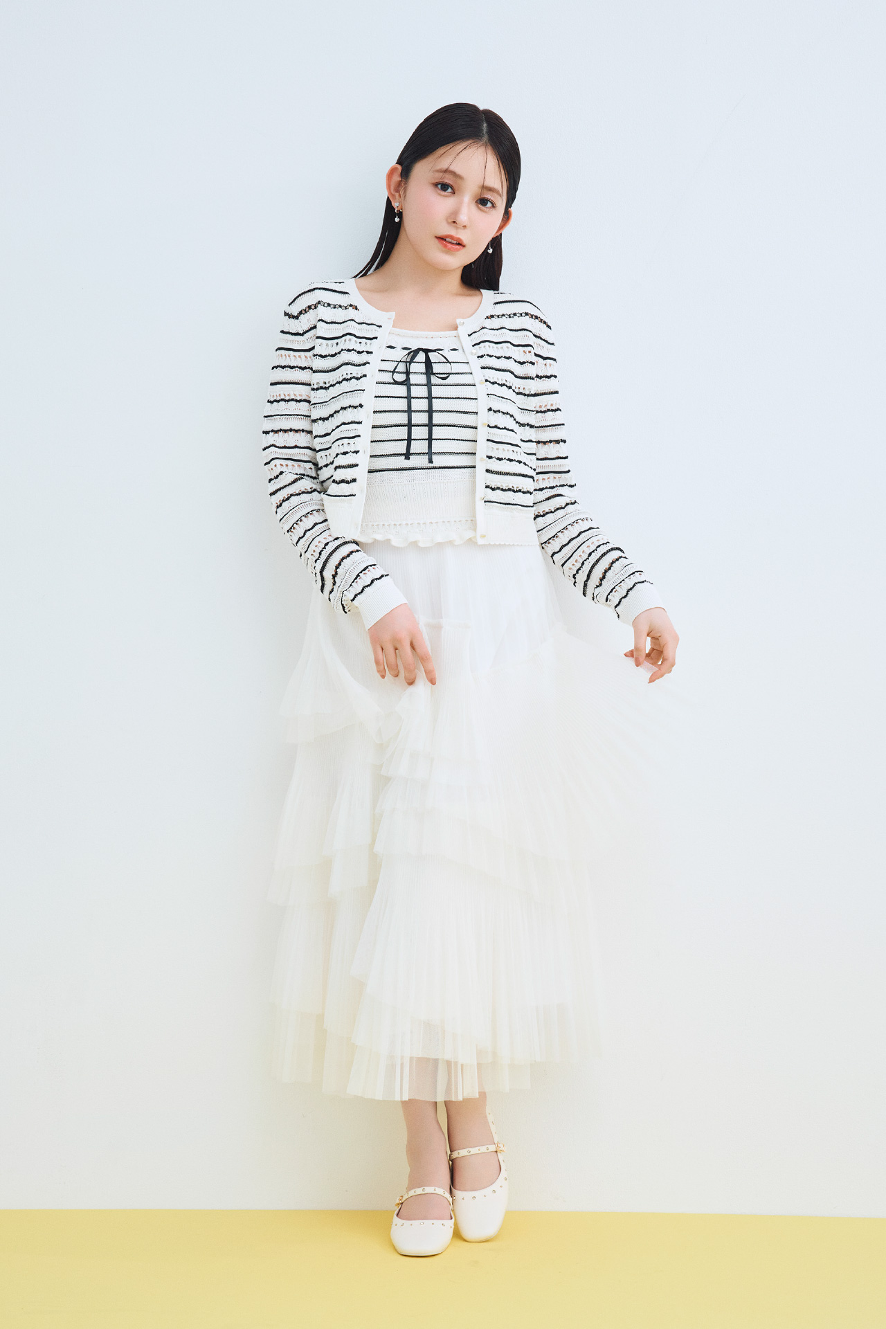 レーシーニットアンサンブル、ランダムチュールプリーツスカート、ハートパヴェビジューイヤリング、ビジュースタッズフラットシューズを着用した女性のイメージ