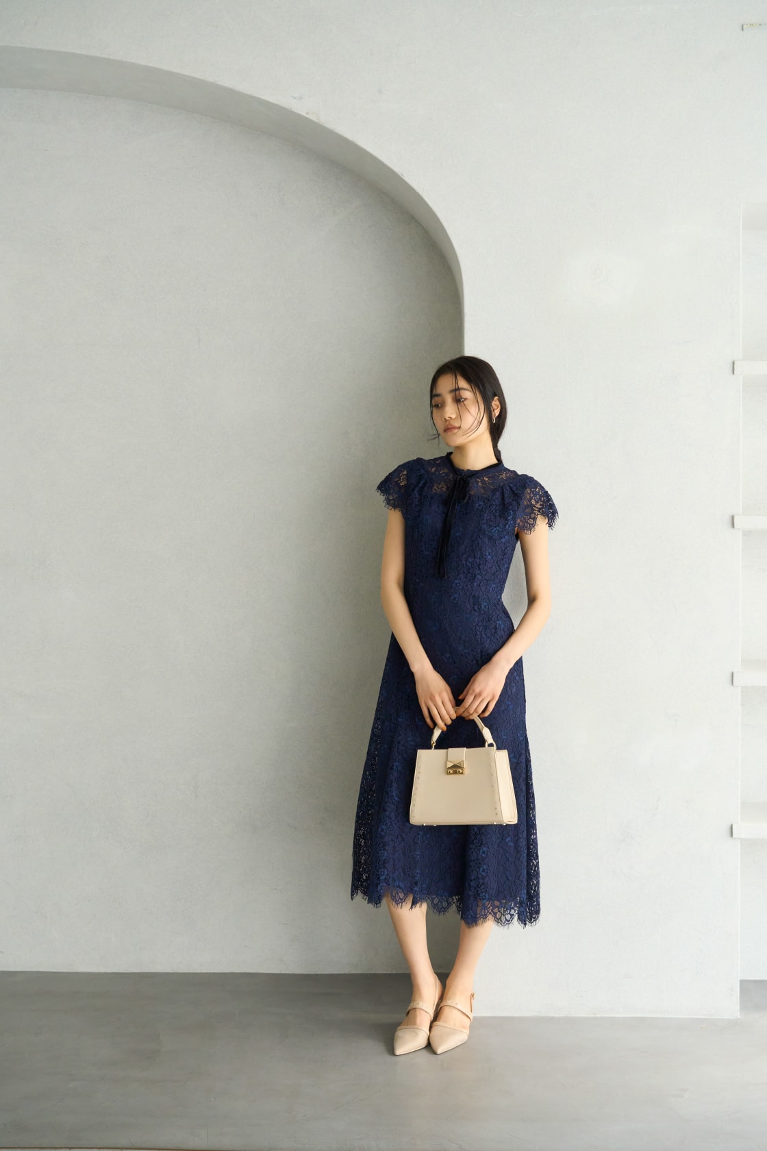 ベージュのバッグを持ちネイビーのワンピースを着た女性が左下を向いている画像