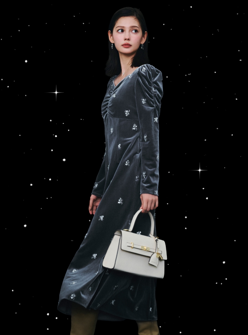 グレー色の花柄刺繡ベロアワンピースとアイボリー色のビジューツイストバックルハンドバッグを着用した女性のイメージ