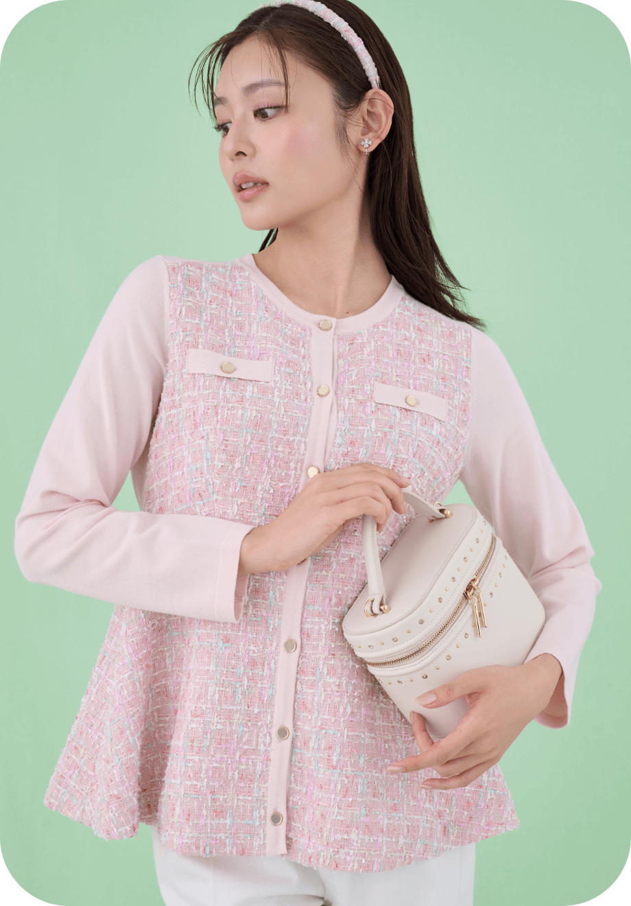 ピンク色のツイードペプラムカーディガンとロゴメタル付きツイードカチューシャ、アイボリー色のリュタンビジュースタッズバニティバッグを着用した女性のイメージ