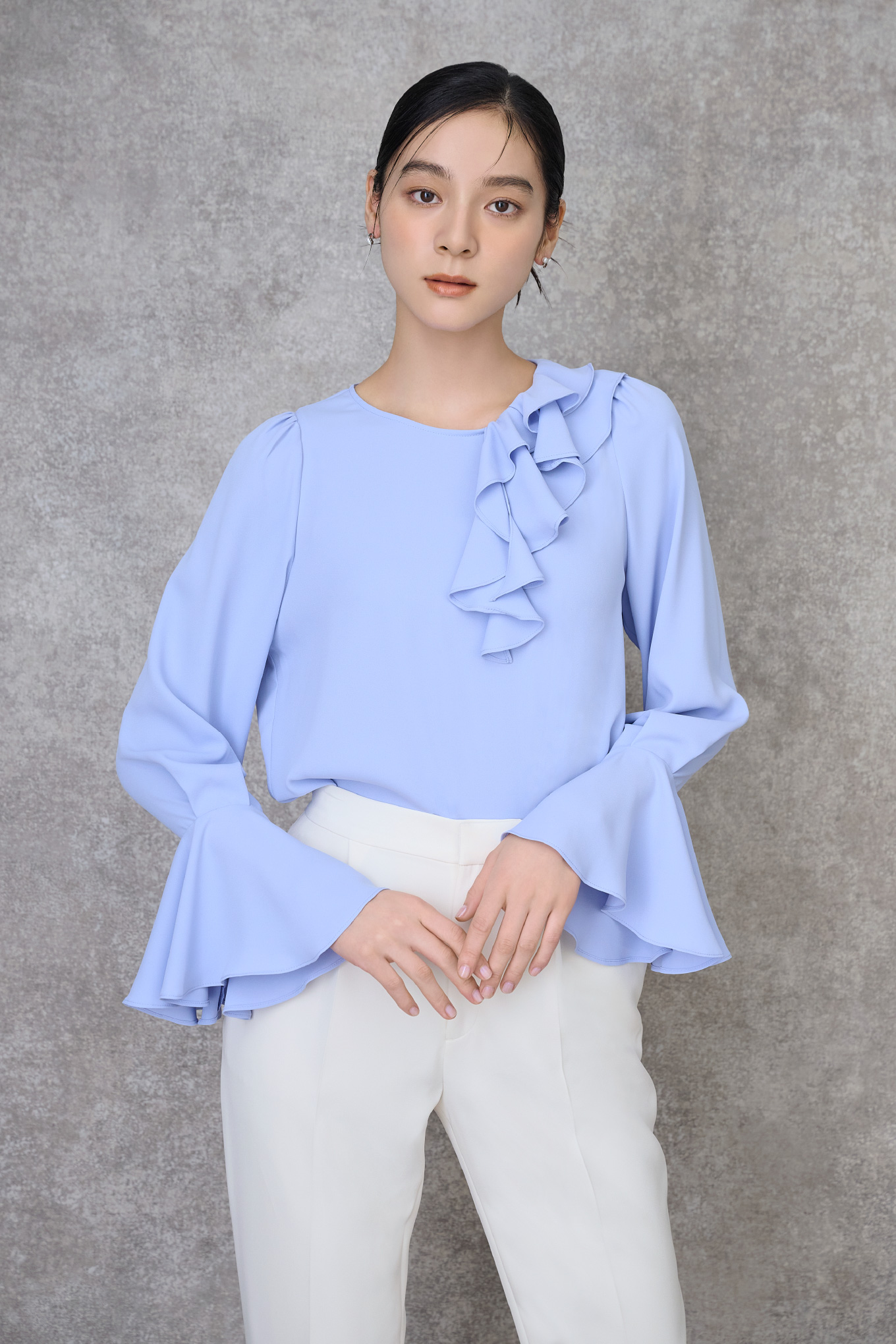 青色のアシメラッフルブラウス、アイボリー色のテーパードパンツを着用したモデル画像