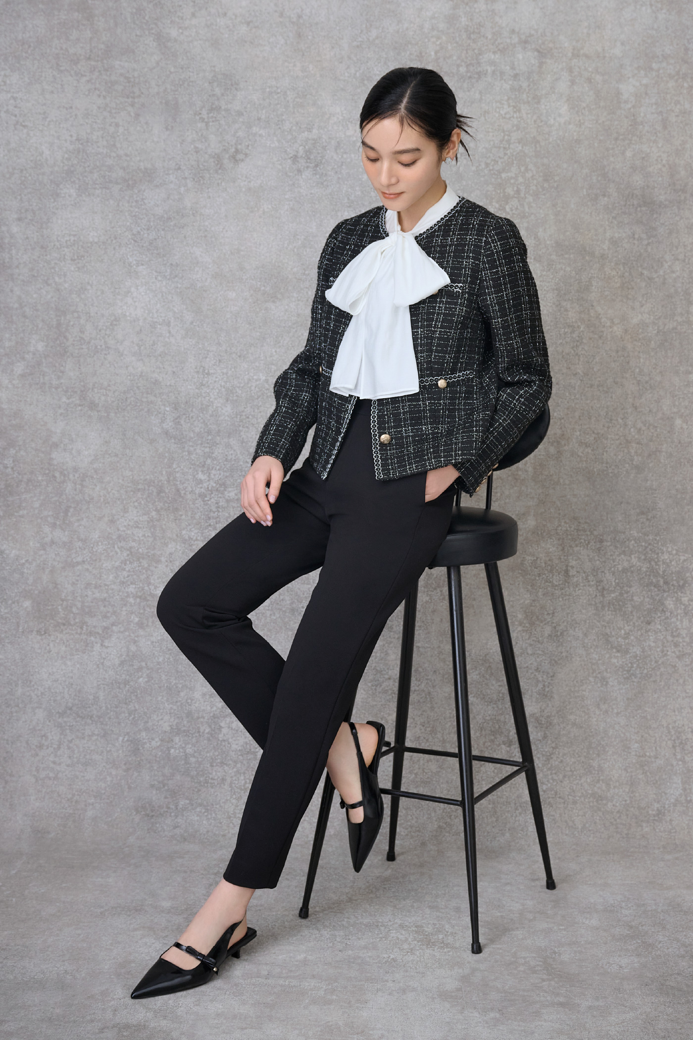 ブラック色のミドル丈ノーカラーツイードジャケットとストレッチスキニーテーパードパンツ、リボンディテールバックストラップミュール、白色のビッグリボンセミシアーブラウスを着用したモデル画像