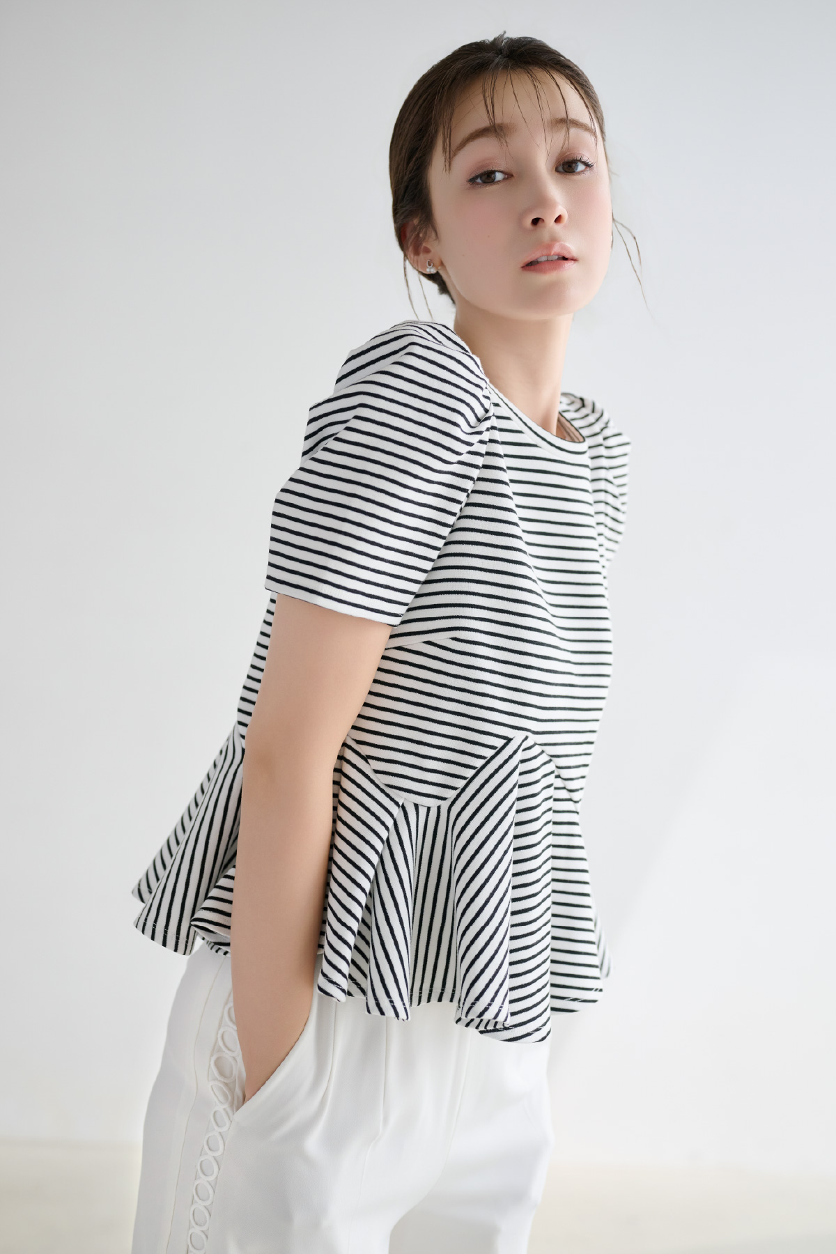 ストライプ柄のアシンメトリーカットトップス、レースラインワイドストレートパンツ、Cロゴビジューパールプチピアスを着用した女性のイメージ