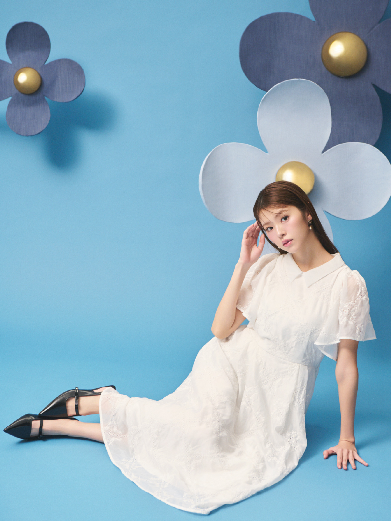 フラワーエンブロイダリーワンピースとCロゴガラスパールリボンピアス、リボンディテールバックストラップミュールを着用して床に座ってる女性のイメージ