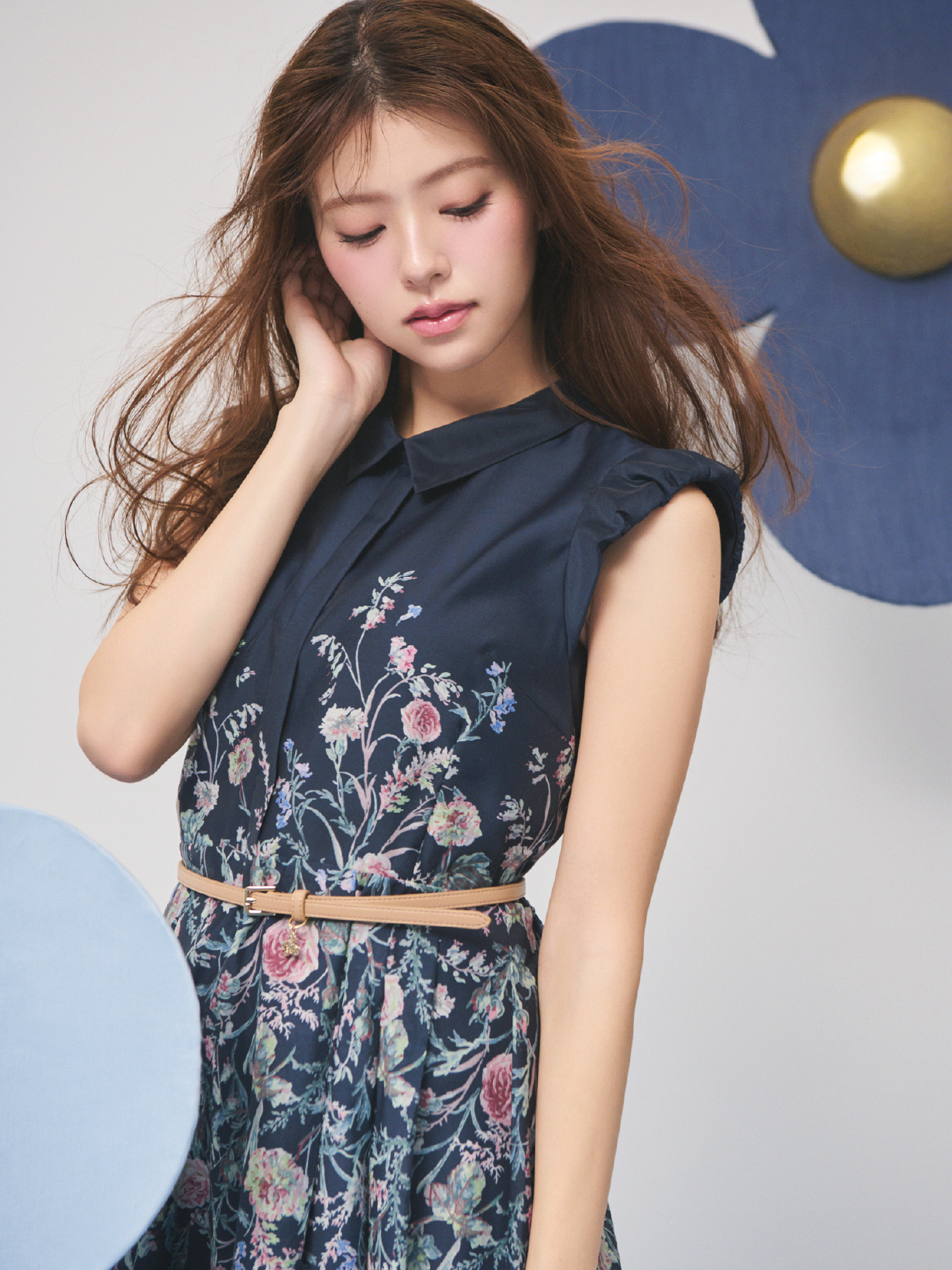 ネービー色のパネルフラワーワンピースとキャメル色のカリグラフィーチャーム付きナローベルトを着用した女性のイメージ