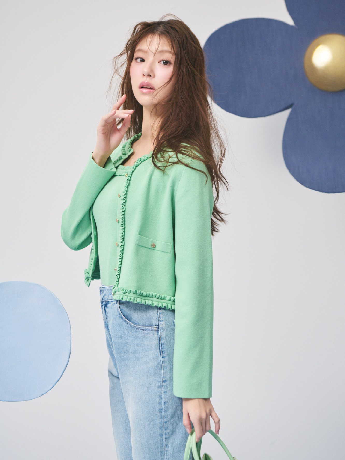 エメラルド色のフリルトリムニットアンサンブル、ハイウエストフレアデニムパンツを着用したモデル画像