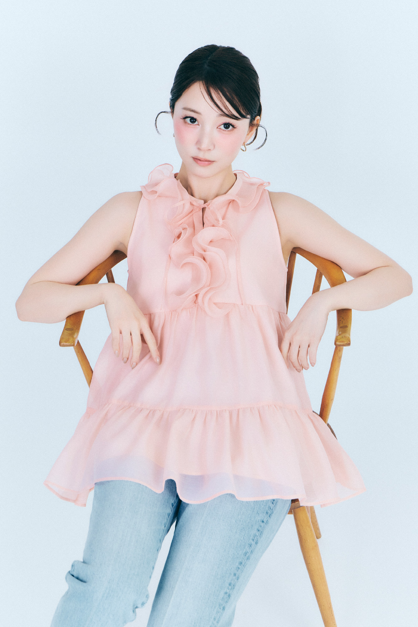【WEB限定カラー】ラッフルフリルネックブラウスとデニムテーパードパンツを着用して椅子に座ってるモデル画像