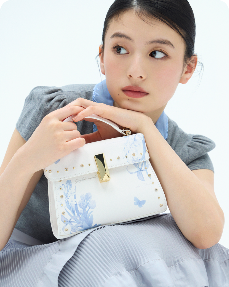 【REDOUTE】衿付きニットプルオーバー、【洗える】クリスタルティアードスカート、【P.J. REDOUTEコラボ】リュタンビジュースタッズフラワープリントバッグを着用した女性のイメージ