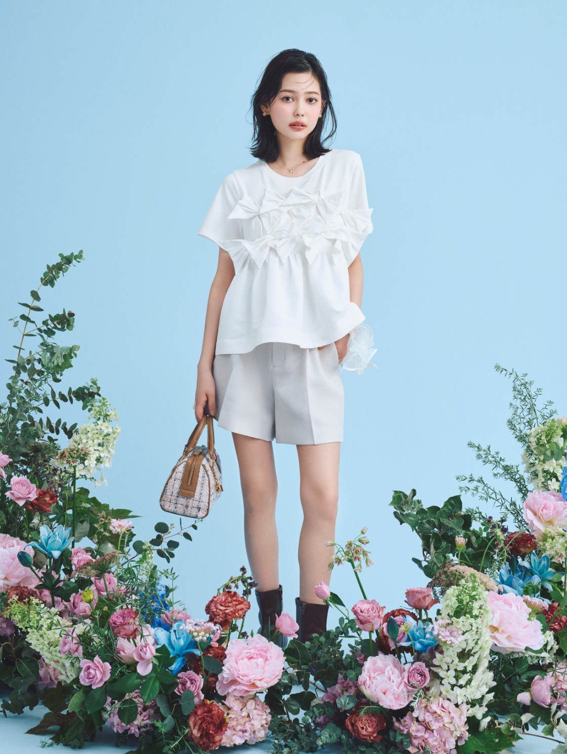 【HANAE MORI×CELFORDコラボ】バタフライリボンチュニック、【洗える】ベルト付きカラミショートパンツ、メタルチャームツイードミニボストンバッグ、ポインテッドストレッチショートブーツを着用してソファーに座ってる女性のイメージ