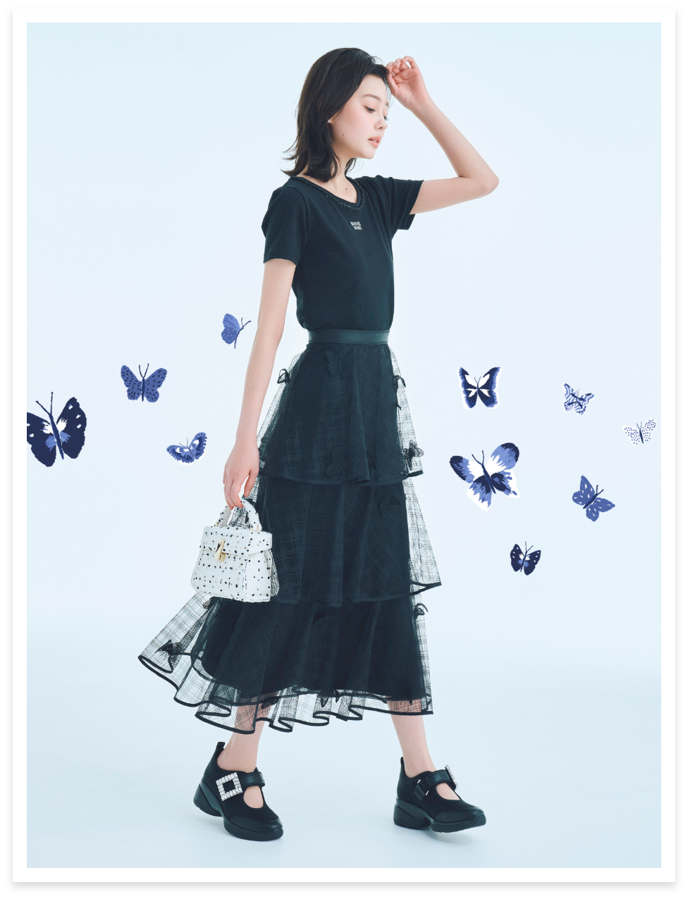 黒色の【HANAE MORI×CELFORDコラボ】ロゴカットトップス、【HANAE MORI×CELFORDコラボ】バタフライモチーフティアードスカート、ビジュースタッズツイードポシェットを着用したモデル画像